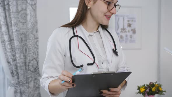 Woman Doctor Writes Out the Appointment of a Patient Lying on a Bed in a Hospital Ward