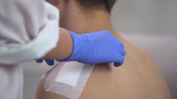 Nurse Hands Taking Off Adhesive Bandage From Scratched Shoulder of Male Patient