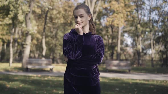 Portrait of Charming Young Woman Standing in Sunlight Outdoors and Smiling at Camera