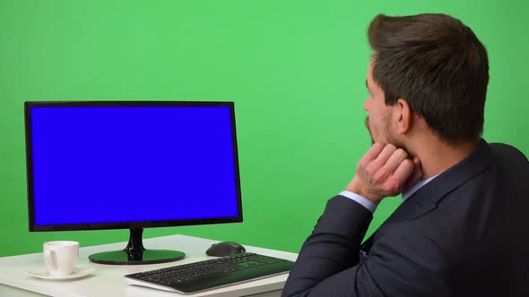 A Young Businessman Sits at a Desk and Looks at a Desktop Computer, Bored - Green Screen Studio