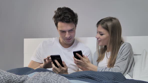 Young Couple Sharing Information While Using Smartphone in Bed