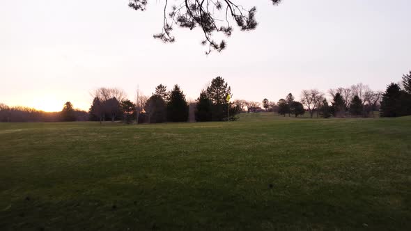 Golf course at sunrise. Dolly forward from treeline revealing yellow flag on green. Golden yellow hu