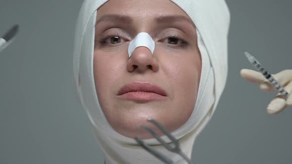 Surgery and Injection Instruments in Front of Woman Face in Elastic Bandage