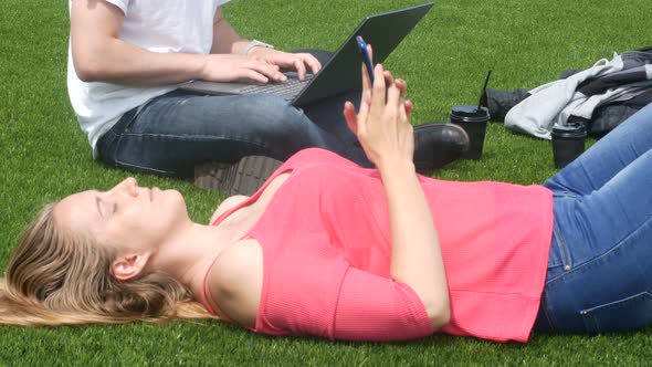 A Guy And A Girl Are Relaxing On The Lawn And Using Gadgets