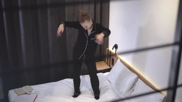 Joyful Dance of Carefree Caucasian Teenage Girl on Bed. Wide Shot of Cheerful Beautiful Slim