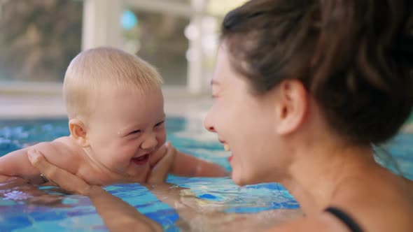 Happy Mother in Red Swimming Suit with Baby Son Surfing Water with Fun in Swimming Pool