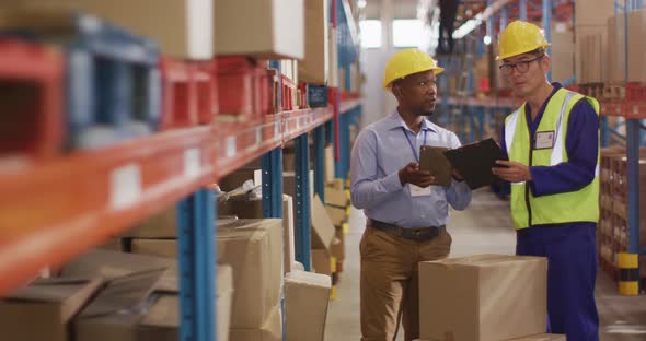 Diverse male workers wearing safety suits and talking in warehouse