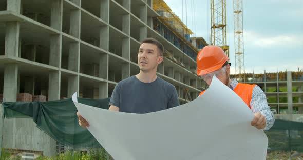 Builder with a Male Client Near Building Under Construction Outdoors. Two Male Builders Engineers