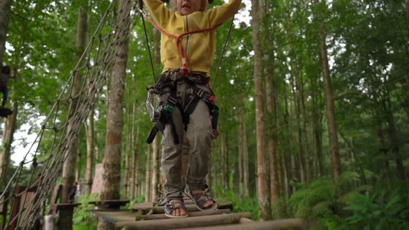 Superslowmotion Shot of a Little Boy in a Safety Harness Climbs on a Route in Treetops in a Forest