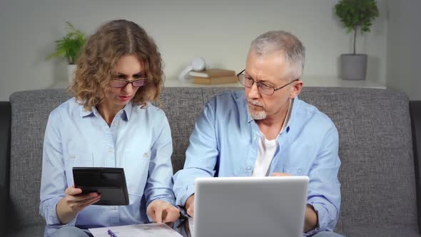 A Middleaged Couple is Doing Calculations on a Calculator and Laptop