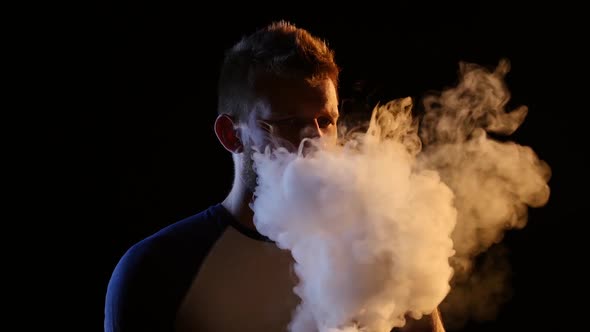 Man Smokes an Ecigarette, Blows Smoke Through His Nose, Black Background