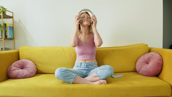 Happy and Cheerful Woman in Pink Tank Top and Blue Jeans Sits on Bright Yellow Sofa at Home and