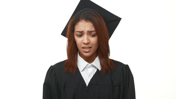 Stressed Young African American Graduate in Black Robe and Square Academical Cap Crossing Her