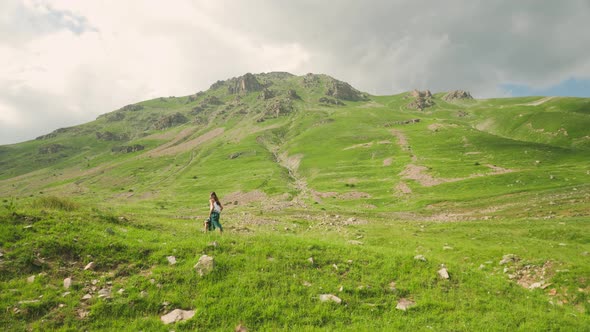 Beautiful woman wearing a green dress walking through a grassy field beneath a mountain in Barcelonn