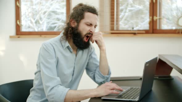 Man Works at Home in Front of the Computer and Yawns From Fatigue or Boredom