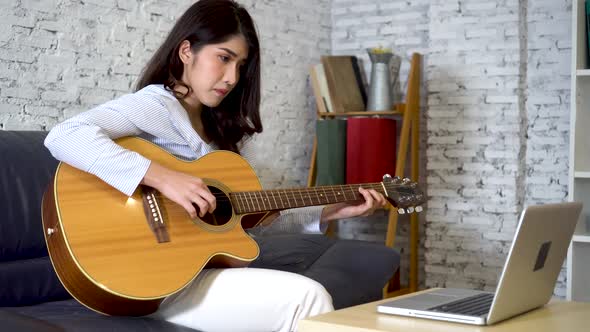 Young Asian Woman Learning How to Play Guitar on Laptop