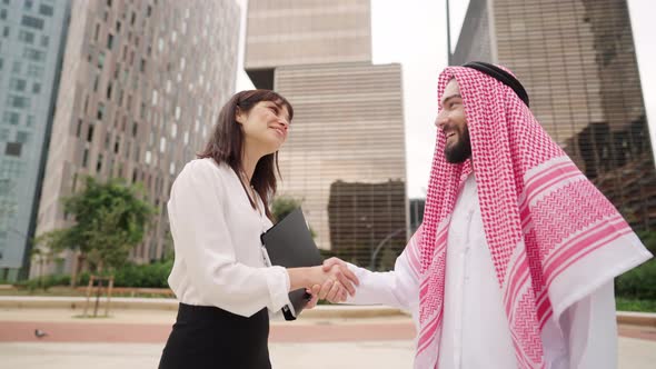 Happy Muslim Arab Man Shaking Hands with Caucasian Female Partner During Meeting Outdoors