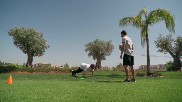 A Young Guy with a Personal Fitness Trainer Performs Pushups and Resistance Runs for Endurance and