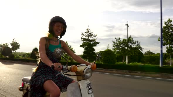 Slow motion clip of beautiful young woman laughing whilst riding her moped.