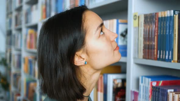 Young Attractive Female Student Looking for the Right Textbook to Prepare for the Exam While