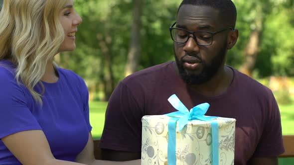 Lady Giving Christmas Gift to African-American Boyfriend While Resting in Park