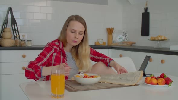 Middle Aged Woman Eating Healthy Breakfast and Reading Newspaper in Kitchen