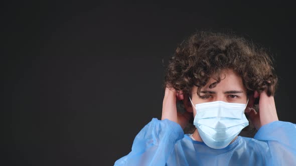 Serious Male Doctor in a Blue Medical Coat Put on a Medical Mask Looking at Camera