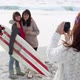 Girl taking photograph of two friends on beach with surfboard - VideoHive Item for Sale