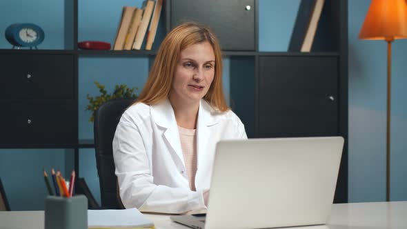 Doctor Woman Listening To Patient Having Laptop Web Chat Sitting at Table in Clinic Office