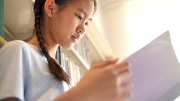 Asian teenager student reading a book in school library.