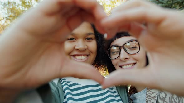 Portrait of Happy Young Women Friends Showing Heart Gesture with Hands Smiling