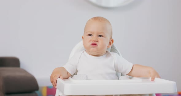 Portrait of Young Baby in White High Baby Chair Who Makes Funny Faces and Grimaces White Walls on