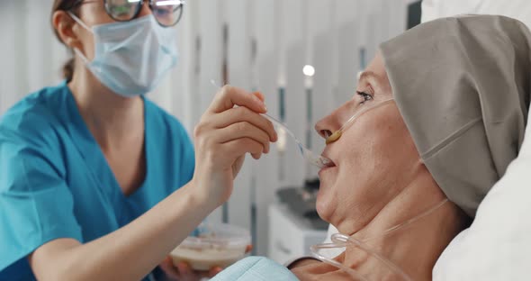 Nurse Wearing Safety Mask Feeding Sick Senior Woman in Hospital