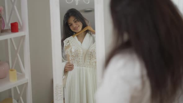 Reflection in Mirror of Smiling Happy Middle Eastern Bride Trying on Wedding Dress in the Morning