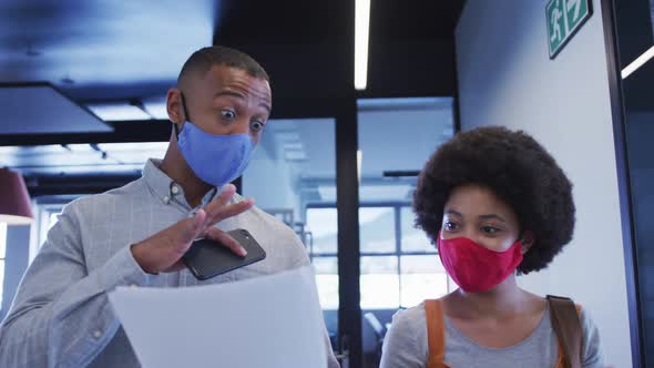 Diverse business people wearing face masks walking and using digital tablet in modern office