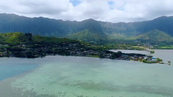 Aerial over Kaneohe Bay towards lush green mountains with moving cloud cover in East Oahu, Hawaii