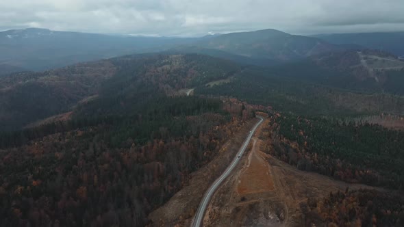 Aerial View of Countryside Mountain Road in Green and Brown Forest Against Mountains Drone Moving