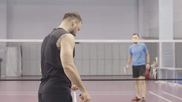 Back View of Tattooed Caucasian Sportsman Competing in Badminton with Young Blurred Man at the