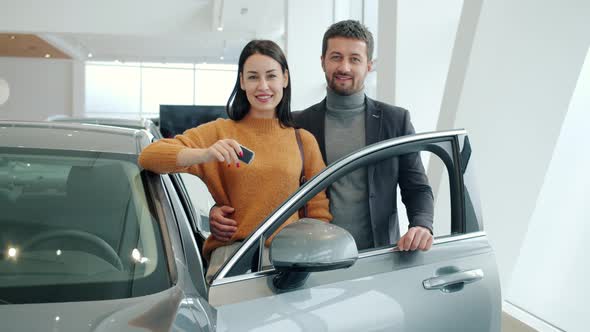 Portrait of Man and Woman Standing Near Beautiful New Car in Showroom Smiling