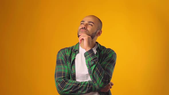 Thinking Man Looking Up and Touching His Chin Against Yellow Background