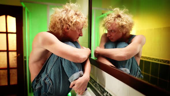 Scared Depressed Queer Man Sitting in Bathroom Looking at Reflection in Mirror