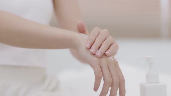 Close up woman hands pushing pump plastic lotion bottle applying moisturizing cream on hands.