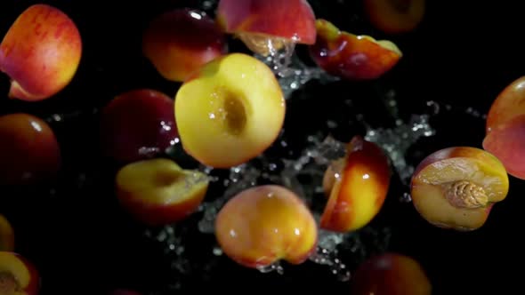 Halves of a Fresh Peach are Bouncing in Splashes of Water on a Black Background