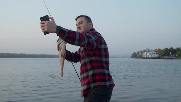 Male Angler Taking Selfie with Fish Near Water