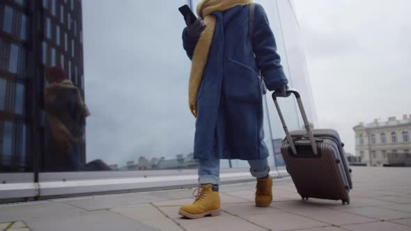 Female Tourist Walking with Luggage and Using Smartphone in City