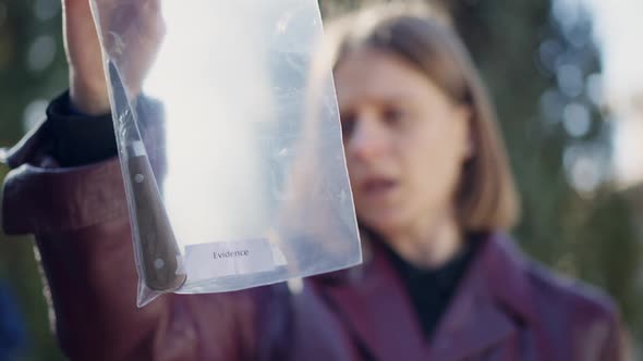 Closeup Knife Evidence in Transparent Plastic Bag with Blurred Concentrated Woman at Background