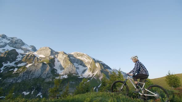 Mountain biker stops to look at abrupt hill from a ridge at sunrise