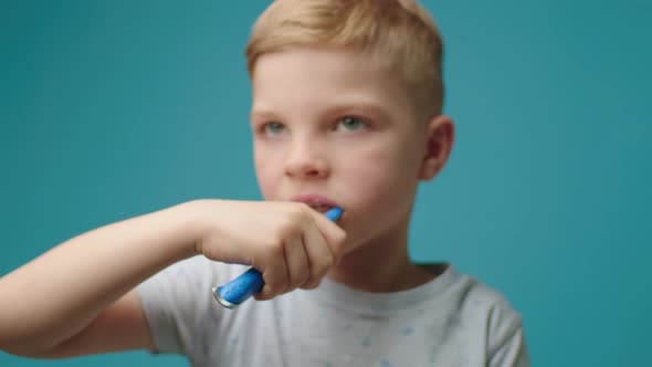 Portrait of Young Boy Brushing Teeth Standing on Blue Background
