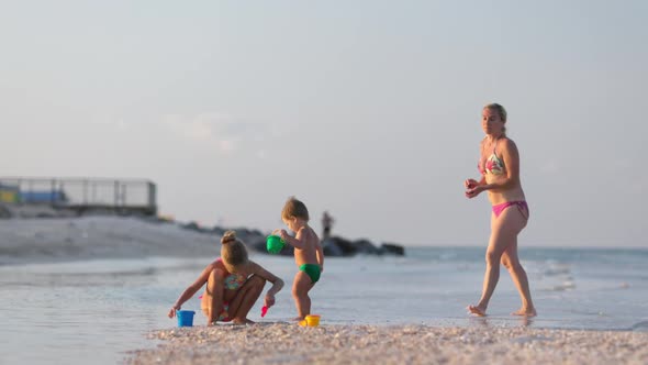 Mom Plays with Her Children Daughter and Baby Building Beads and Castles Decorating Them with Shells