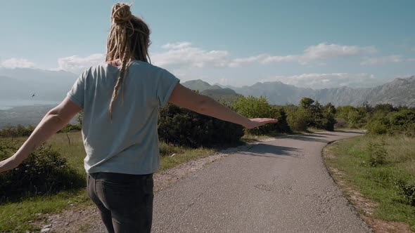 Back view of dreadlocks woman longboarding on mountain background riding skateboard